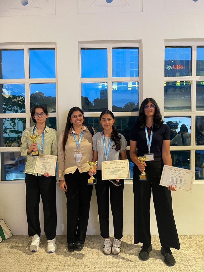 Three students holding Best Project Award trophies and certificates, with a teacher, in Singapore