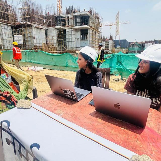 Two volunteers working on laptops at a table on a construction site